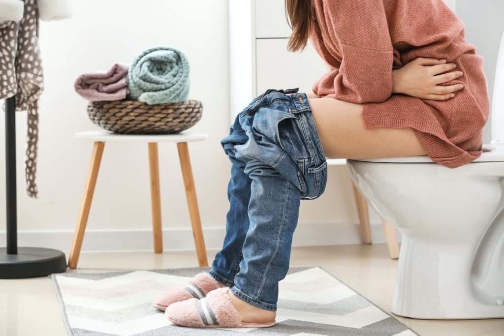 ibs pain: woman sitting on toilet bowl in restroom