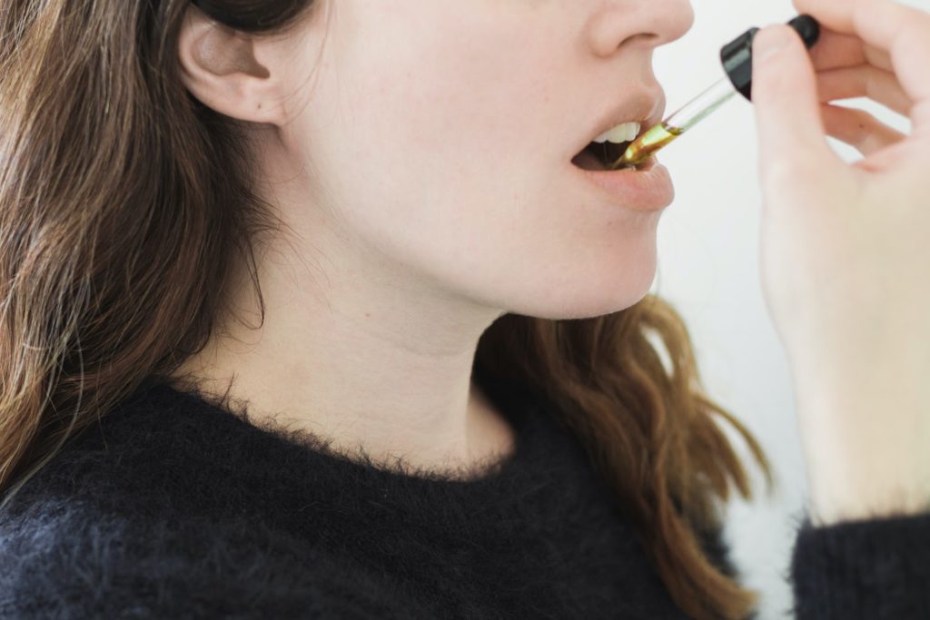 Woman ingesting a drop of oil under her tongue