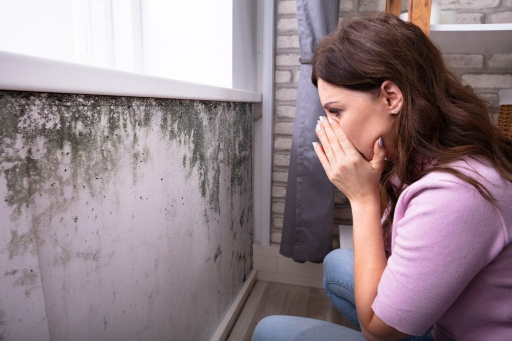 mold toxicity: Shocked woman looking at mold on her wall