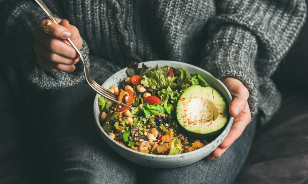 Woman holding a fork and a bowl of healthy food on her lap