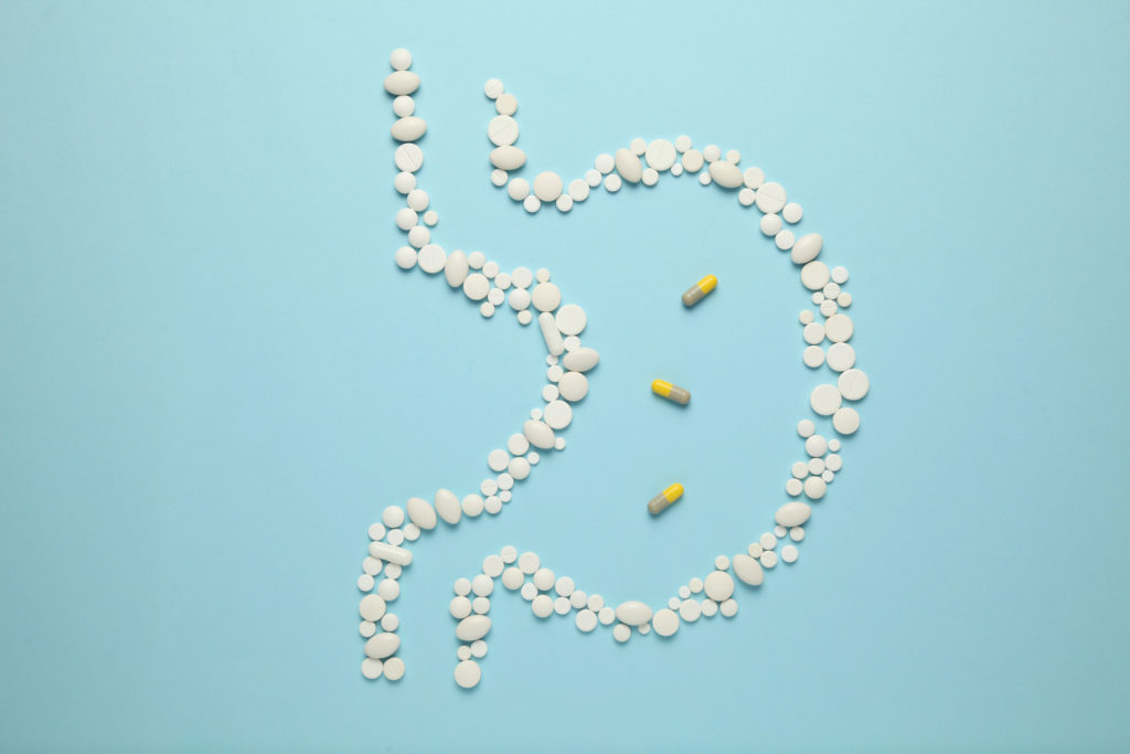 White tablets laid out in the form of a stomach with 3 capsules in the middle