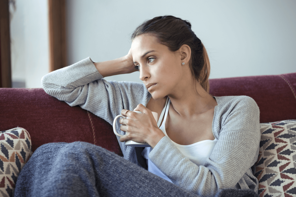 neuroplasticity healing: Woman looking deep in thought while sitting on a couch and holding a coffee mug