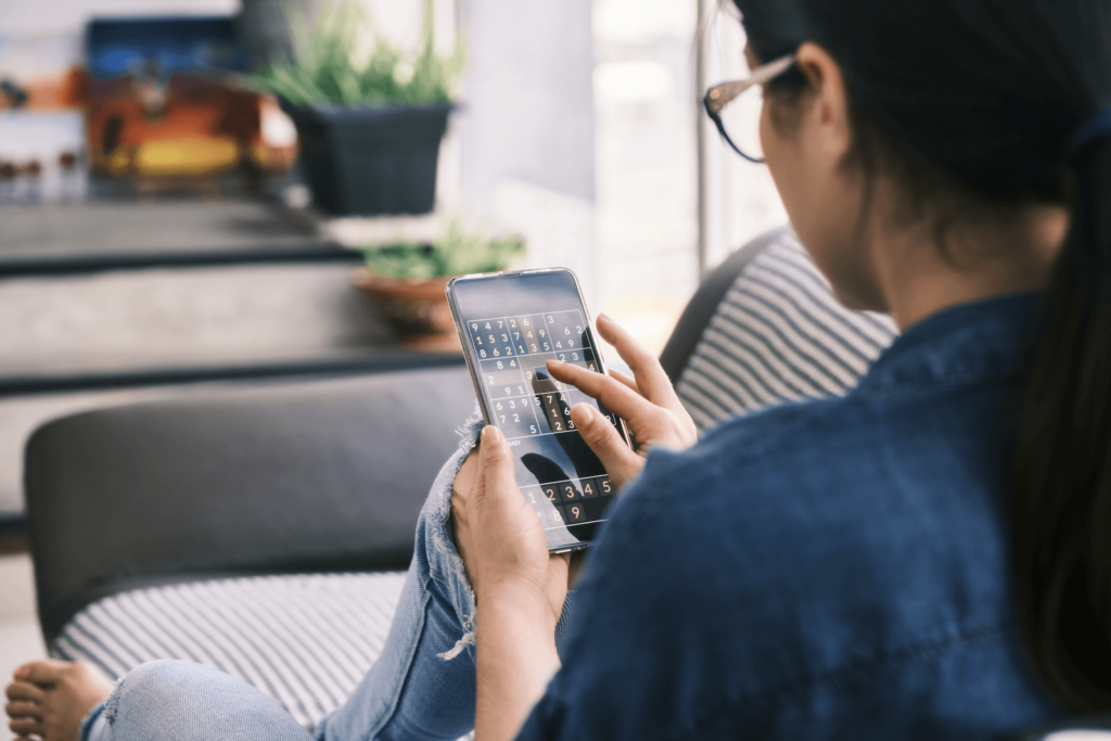 Woman sitting on the couch while playing number games in her mobile phone