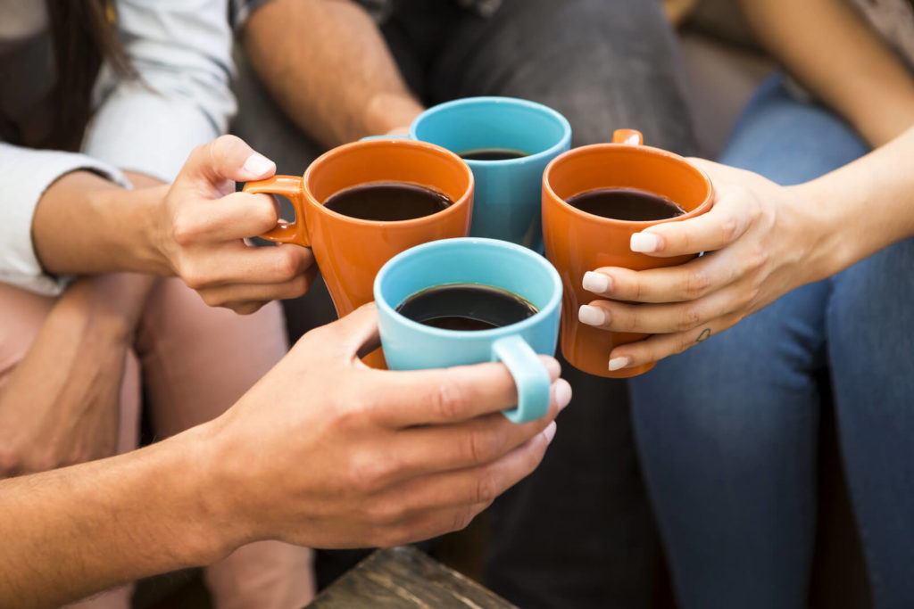 benefits of black coffee: four people clinking coffee mugs