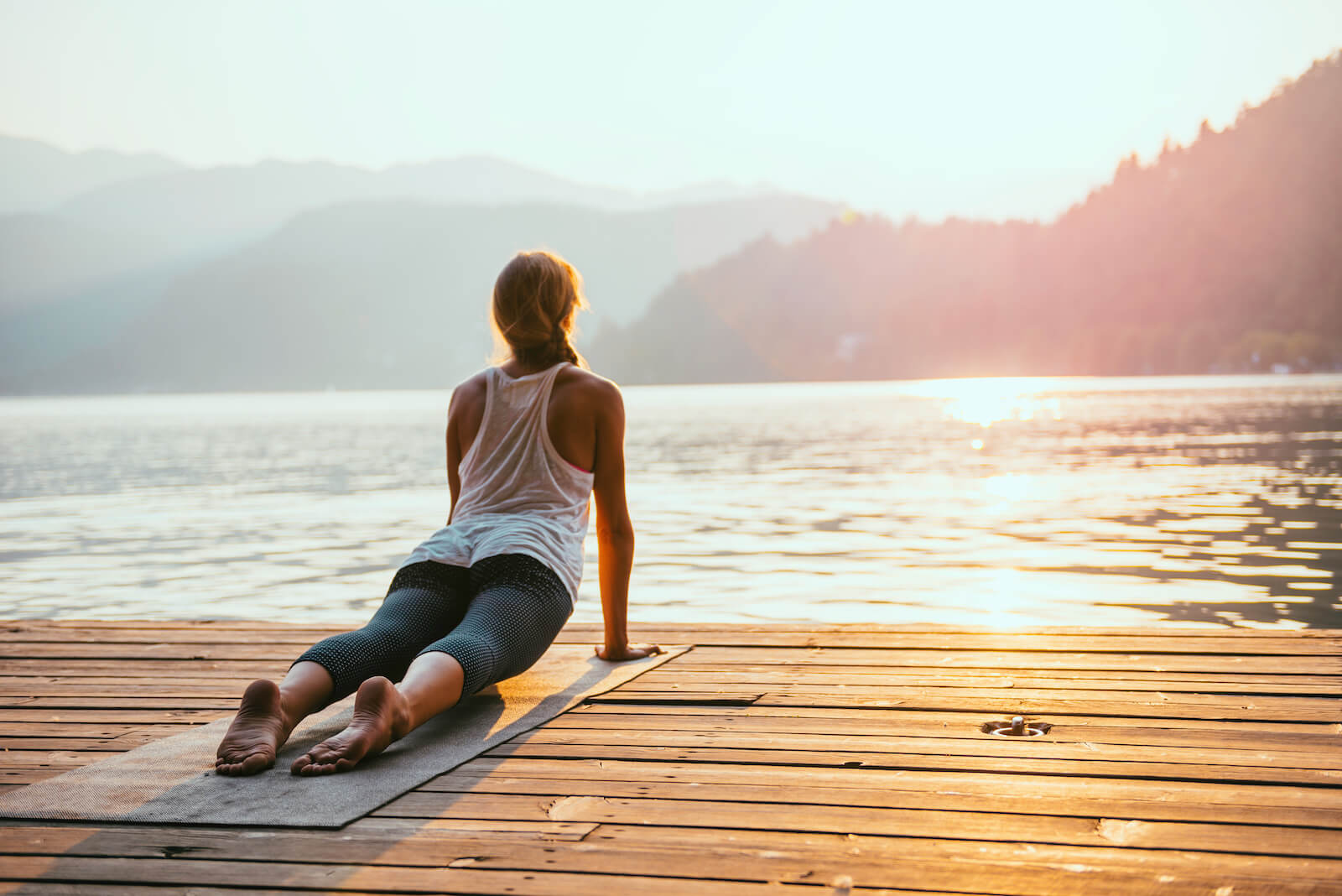 Natural remedies for rheumatoid arthritis: woman practicing yoga by a lake during sunset
