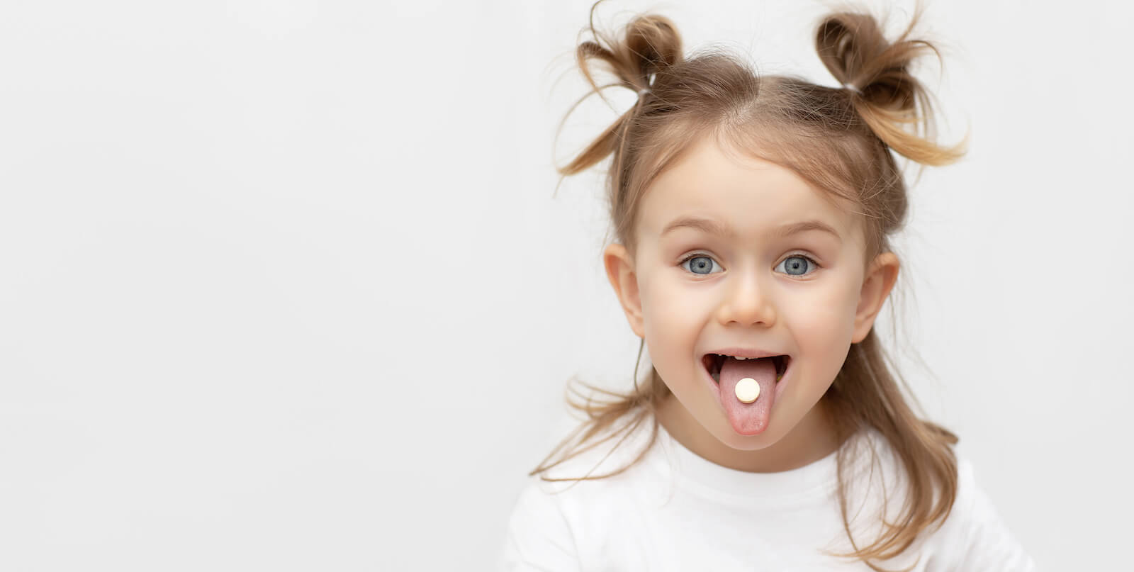 Kids probiotic: little girl showing a pill on her tongue
