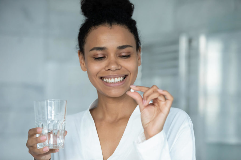 Smiling woman holding a white pill and a glass of water