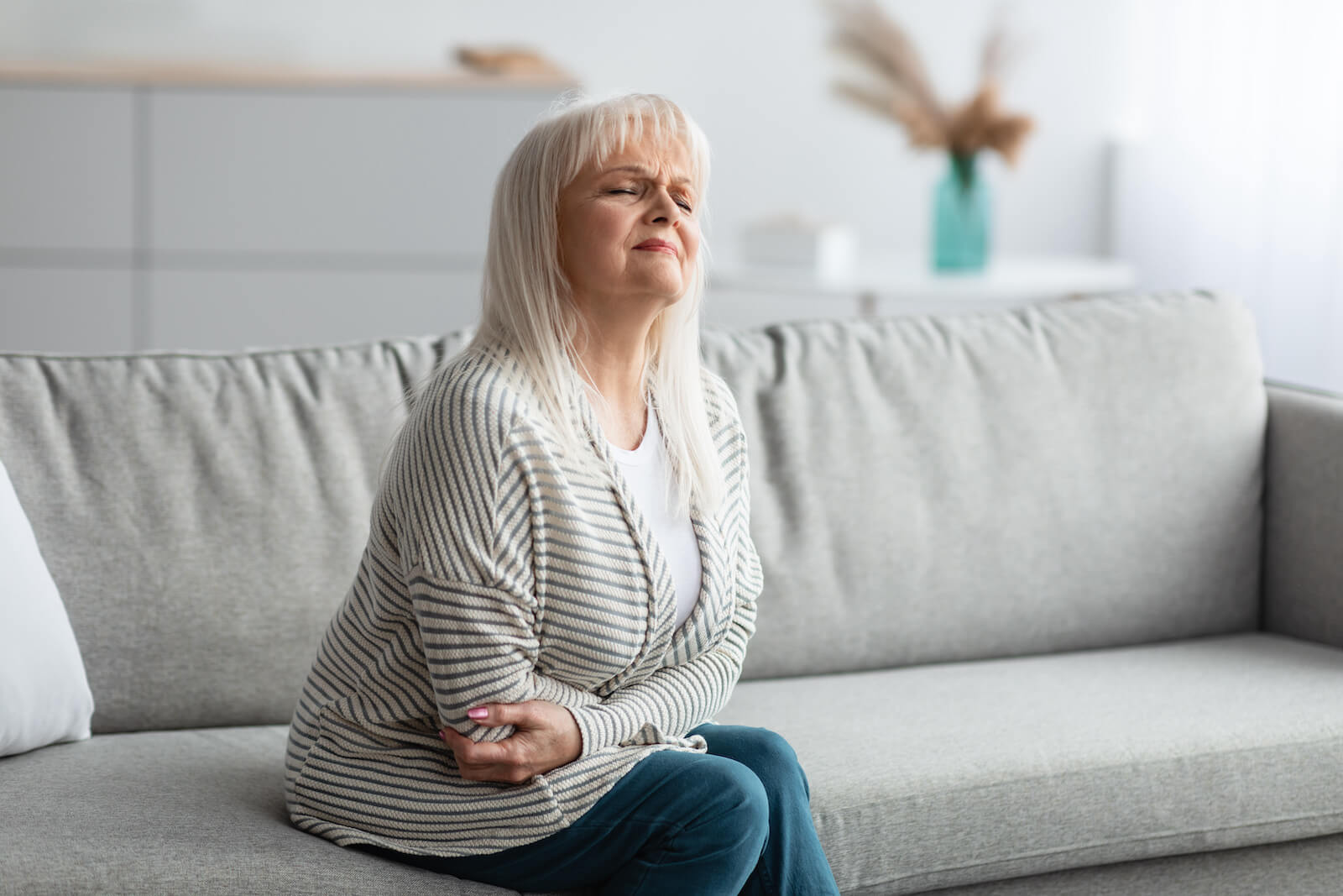 Normal microbiota: elderly woman with a stomachache sitting on a sofa