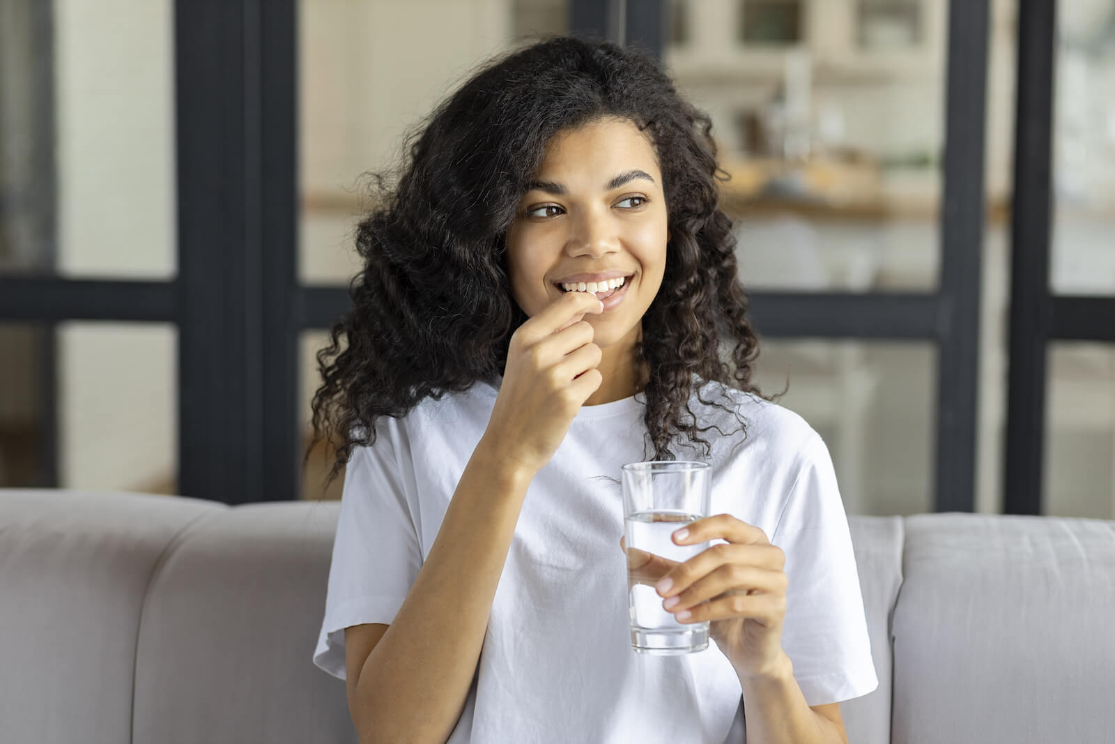 What are the signs you need probiotics: woman about to drink a pill while holding a glass of water