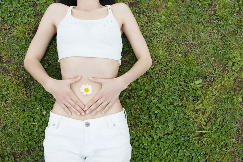 How to get rid of bad bacteria in the gut: woman encasing a flower on her stomach with her hands