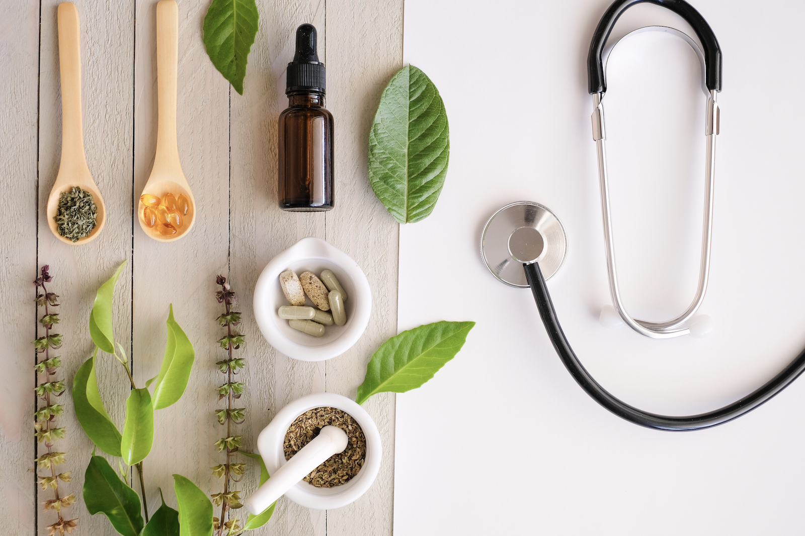 Medicine and herbs on a wooden surface and a stethoscope on a white surface
